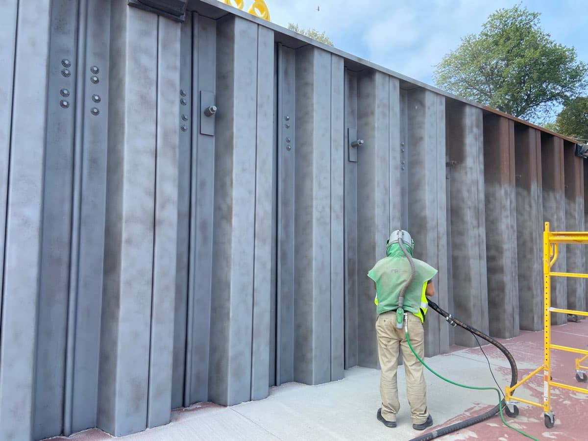 Worker sandblasting large commercial steel wall structure