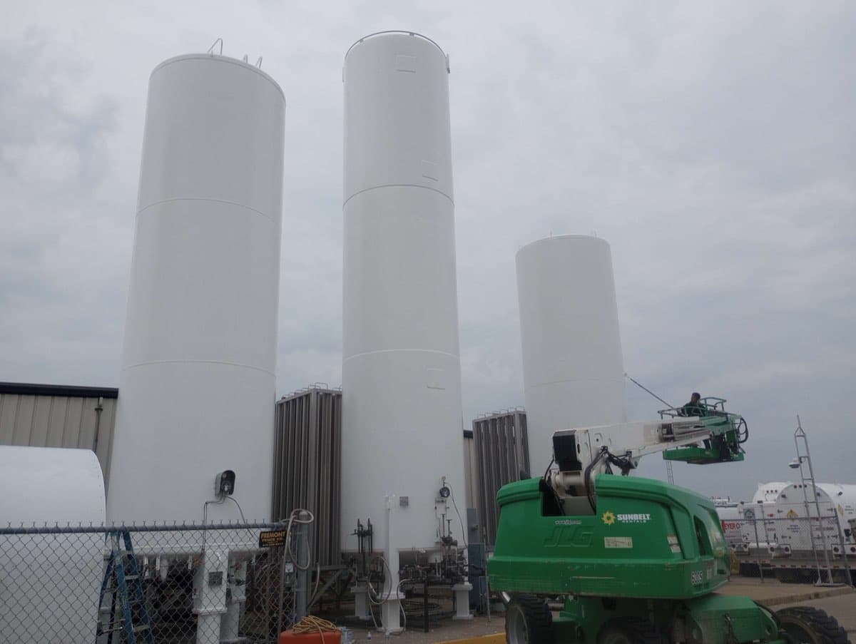 Tall vertical storage tanks being painted by Markley's Precision crew with boom lift